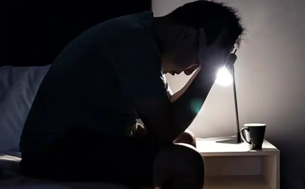 man sitting on the edge of his bed with his head in his hands struggling with depression